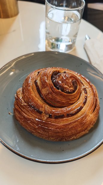 新鲜出炉的肉桂糕点，拥有金黄酥脆的层次，盛放在陶瓷盘上，旁边放着一杯水。这张图片代表了早餐的放纵、咖啡馆的氛围和简单的日常乐趣。图片下载