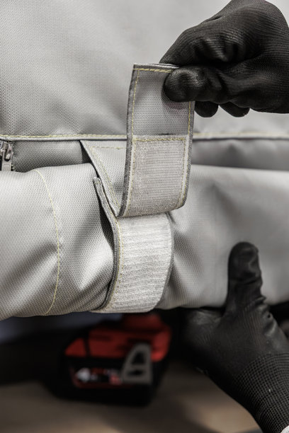 戴着手套的手在仓库环境中固定卷起的灰色工业织物罩上的大型魔术贴搭扣，重点展示了固定机制和耐用纺织品图片下载