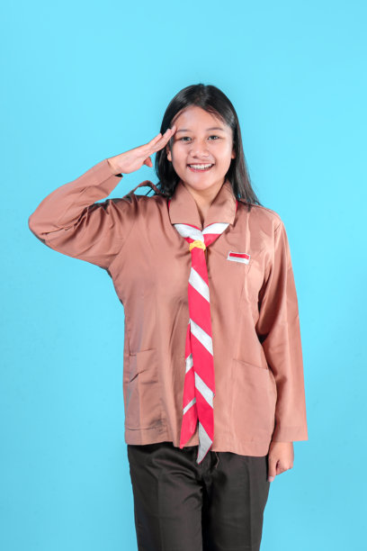 一位面带灿烂笑容、身穿童子军制服的快乐小女孩正在敬礼，展现出自信和自豪，图片背景为蓝色，适合广告宣传。图片下载