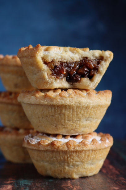 特写镜头，两叠三块圣诞肉馅饼，顶部是撒了糖粉的酥皮雪花盖子，牛油曲奇圣诞甜点，缺了一口露出甜肉馅，背景是斑驳的蓝色，焦点在前景图片下载