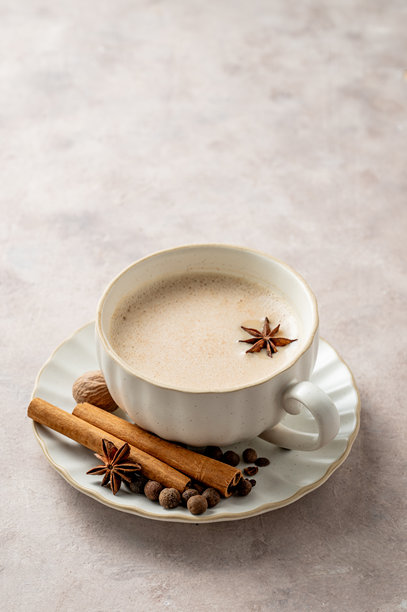 白色杯子里的印度香料奶茶，配有牛奶和香料，置于浅色背景上。图片下载