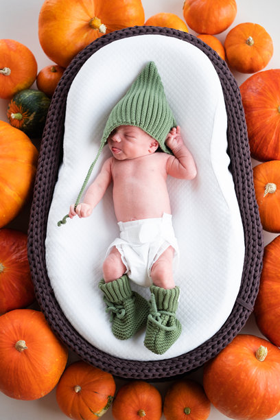 一个新生男婴戴着帽子，睡在装饰着南瓜的棕色摇篮里。万圣节睡着宝宝肖像。竖直照片图片下载