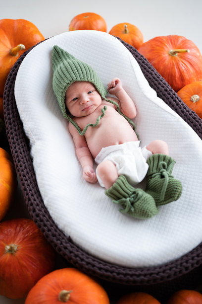一个新生男婴戴着帽子，睡在一个装饰着南瓜的棕色摇篮里。万圣节期间熟睡婴儿的肖像。竖版照片图片下载