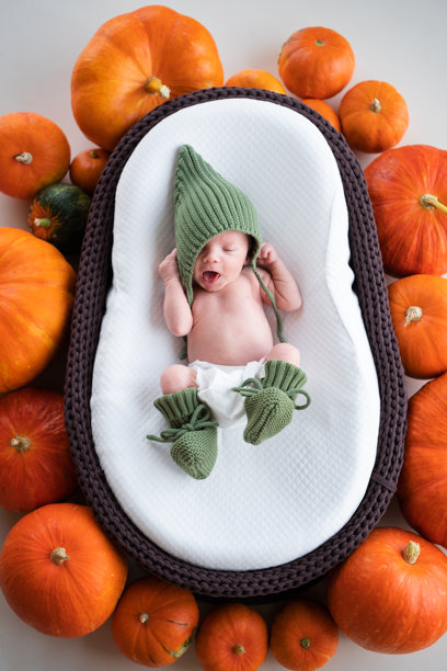 一个新生男婴戴着帽子，在装饰着南瓜的棕色婴儿摇篮里睡觉。万圣节睡着宝宝的肖像。竖版照片图片下载