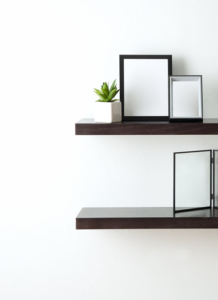 极简风格的深色木质悬浮置物架，安装在白色墙壁上，上面摆放着空白画框、一盆多肉植物和一张玻璃相框照片。图片下载