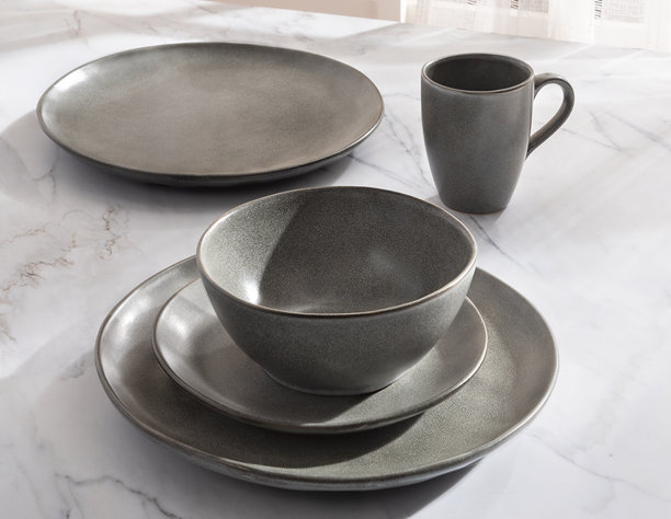 一张戏剧性的特写照片，展示了一套质朴、纹理分明的灰色炻瓷餐具，放置在白色大理石台面上，并以自然侧光和深邃的阴影突出。图片下载