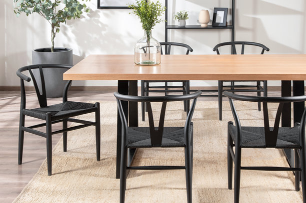 一张现代简约餐厅内部的照片，以一张天然浅木色餐桌搭配几把经典的黑色Y型椅和一张天然编织地毯为特色。图片下载