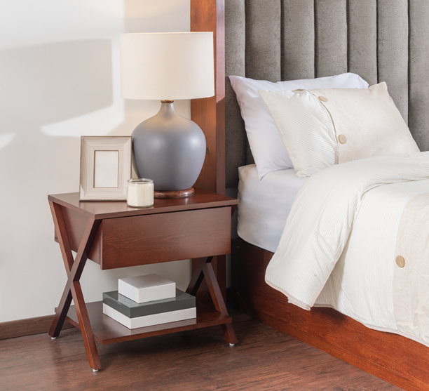 一张现代X型框架深木色床头柜，旁边是一张舒适的床，配有中性色床品和灰色台灯的摄影。图片下载