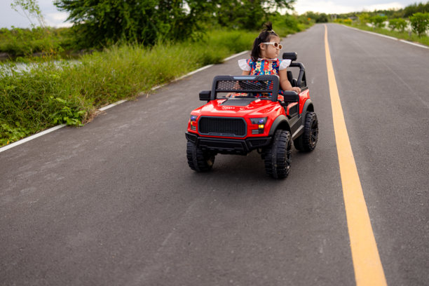 一个可爱的亚洲小女孩坐在一辆玩具遥控车里，停在水泥路上，宝宝坐在车里，对着镜头微笑。图片下载