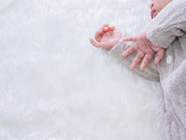 一张近景照片，展示了新生儿戴着灰色毛衣的手，背景是白色的地毯。图片下载