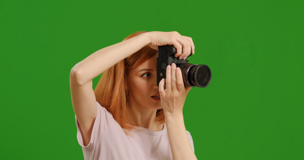 摄影师站在绿色背景前，热情地拍摄照片的侧面视图。图片下载