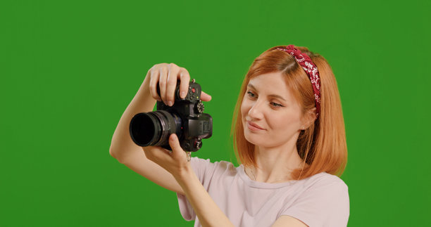女摄影师在演播室的绿色屏幕背景前，看着相机拍摄的照片。图片下载