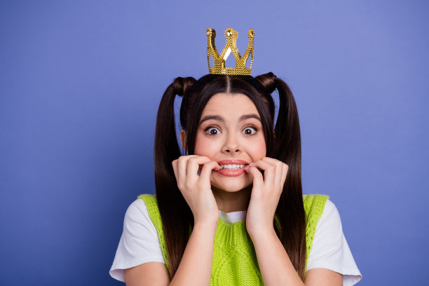 戴着皇冠发带的快乐年轻女子，穿着亮绿色的毛衣，在蓝色背景前俏皮地摆姿势，适合家庭生活和时尚图库照片图片下载