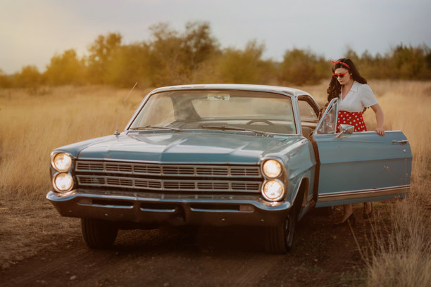 夕阳下，年轻女子在田野里与一辆复古蓝色汽车合影图片下载