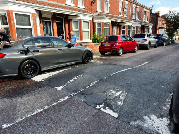 一辆灰色的宝马轿车停在曼彻斯特一条潮湿的街道上，周围是联排房屋和一排汽车。图片下载