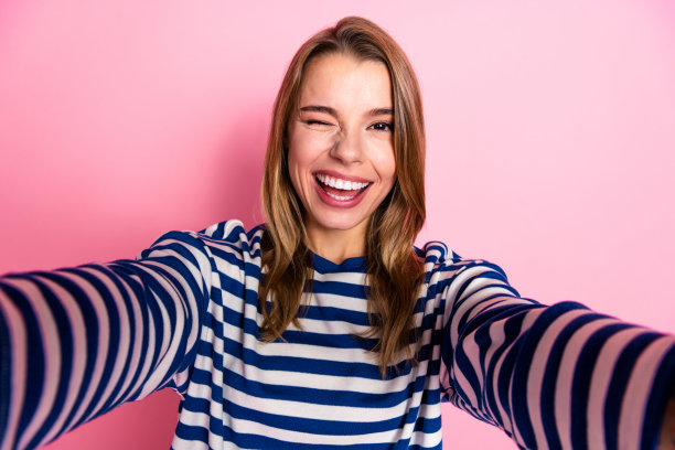 一位身穿休闲条纹毛衣的年轻女子，面带笑容，在纯粉色背景前愉快地摆姿势，适合休闲或生活方式类图片图片下载