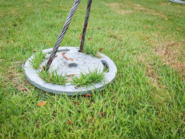 金属地锚板特写，钢缆嵌入草地中。是户外结构、工程、景观或锚固系统的理想视觉素材。图片下载