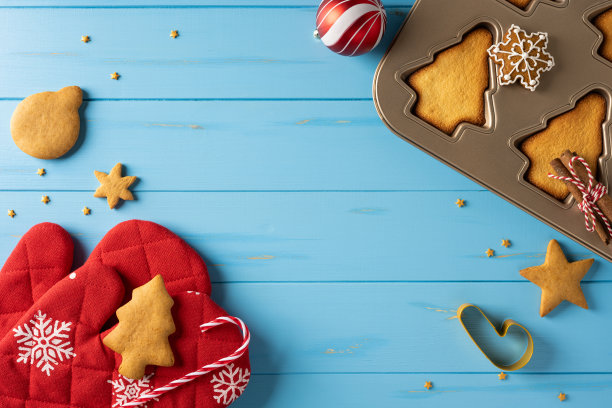 一个充满节日气氛的圣诞烘焙场景，有饼干、金属模具烤盘、拐杖糖和可爱的烤箱手套，背景是明亮的蓝色桌面，非常适合节日庆典、礼品创意和季节问候。图片下载