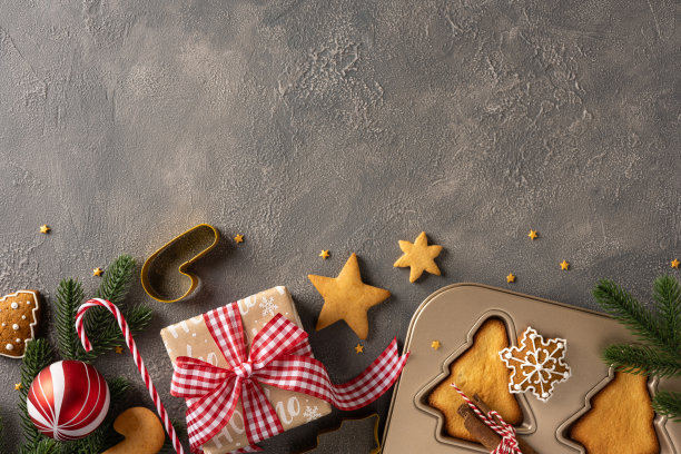 节日氛围的圣诞新年主题摆拍，包含饼干、红丝带礼盒、拐杖糖、饼干模具和常青松枝，整体色调温暖图片下载