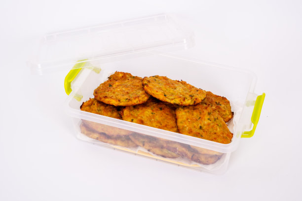 一张特写图片，展示了自制的蔬菜煎饼，整齐地摆放在透明的塑料容器中。金黄酥脆的煎饼外层可以看到香草和蔬菜的碎末。图片下载