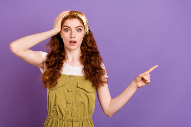 照片：一位惊讶、震惊、难以置信的年轻女士，手指指向虚空，手扶着头部，孤立在紫色背景上图片下载
