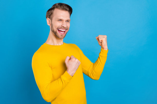 年轻男子的侧面照片，带着快乐积极的笑容，庆祝胜利，像冠军一样，幸运地被隔离在蓝色背景上图片下载