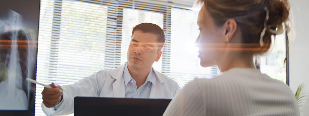 一名身穿病号服的白人男性医生在电脑屏幕上分析医疗结果，旁边有一位女性患者。专业的医疗职业、医疗保健和医药行业、医生与患者的概念图片下载