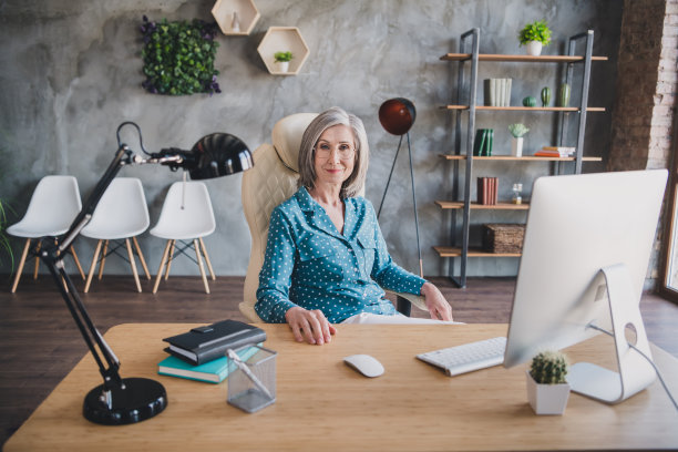 照片：一位美丽、迷人、气质优雅的女士戴着眼镜，在室内工作场所的桌子旁进行远程办公。图片下载