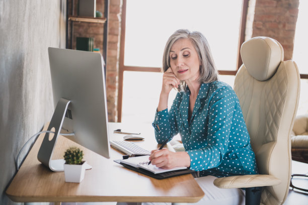 一位年长的女商人侧身坐在办公室书桌前，专注地在笔记本上写下计划待办事项清单的个人资料照片图片下载