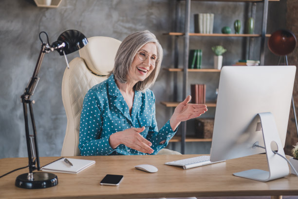 照片：一位快乐、精神矍铄的退休老人，灰发，正在办公室的室内工作站对着网络摄像头交谈图片下载