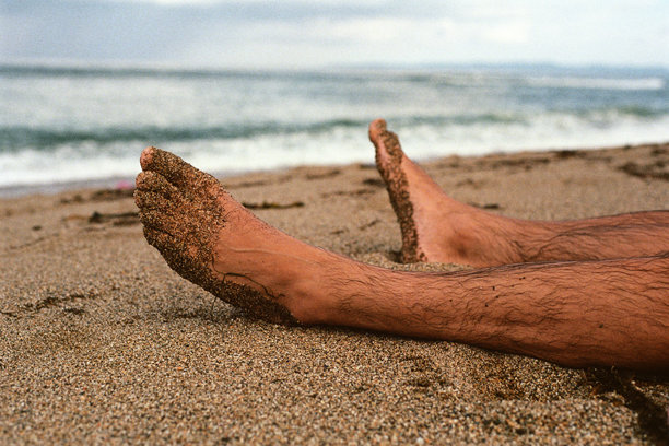 一个人躺在沙滩上，双脚被沙子覆盖。胶片照片图片下载