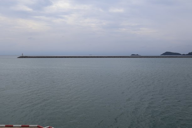 这张照片展示了一片广阔的水域，天空布满云彩，一个码头伸入平静的水中。一座有桩柱的栈桥延伸至水面。图片下载