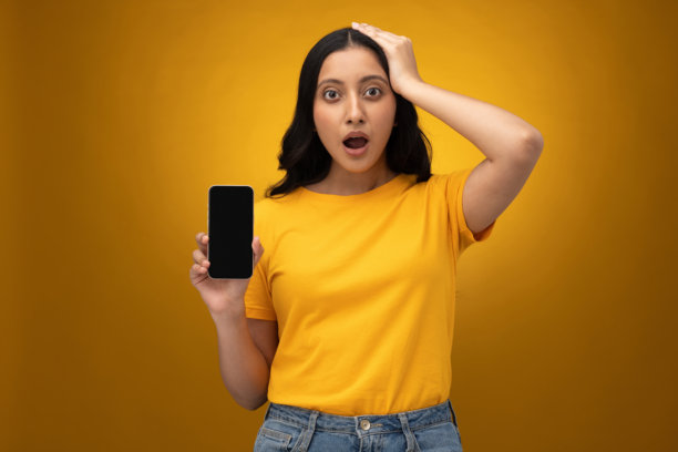 年轻女子展示手机屏幕的图片，孤立在黄色背景上图片下载