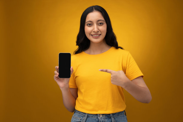 年轻女子展示手机屏幕的特写照片，背景为黄色图片下载