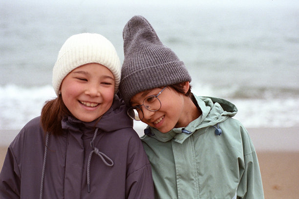 戴着冬季帽子、面带笑容的孩子们在海边。胶片照片图片下载