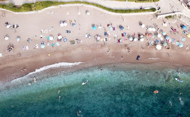 从空中拍摄的无人机照片，展示了圣斯特凡（Sveti Stefan）海滩上色彩缤纷的遮阳伞和碧绿的地中海。图片下载