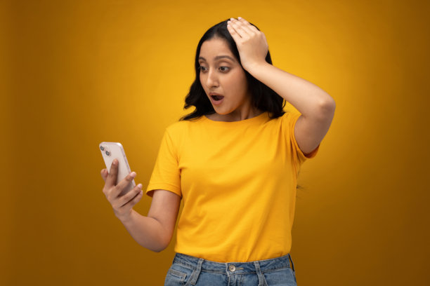 年轻女子使用手机的图片，孤立在黄色背景上图片下载