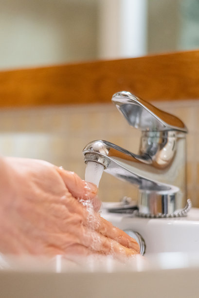 一个人在干净的浴室环境中，在铬制水龙头流出的新鲜水流下洗手，以确保良好的卫生习惯并促进健康图片下载