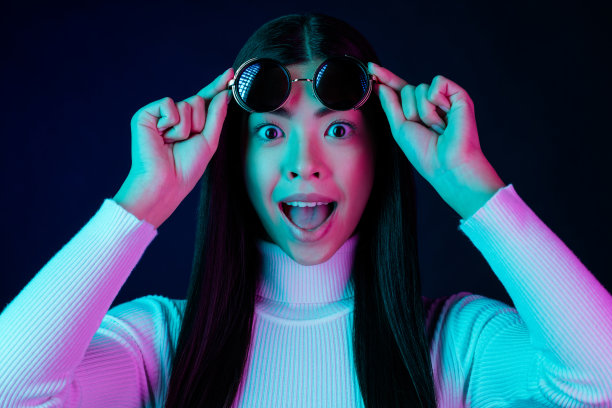 一名年轻女子戴着眼镜，张着嘴，穿着白色毛衣，在黑色深色背景下，举起双手欢呼的照片图片下载