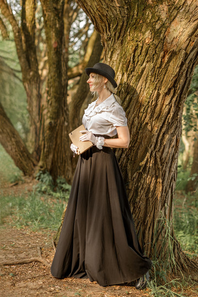 森林里一位身着维多利亚时代服饰的金发美女手持书籍，复古风格图片下载