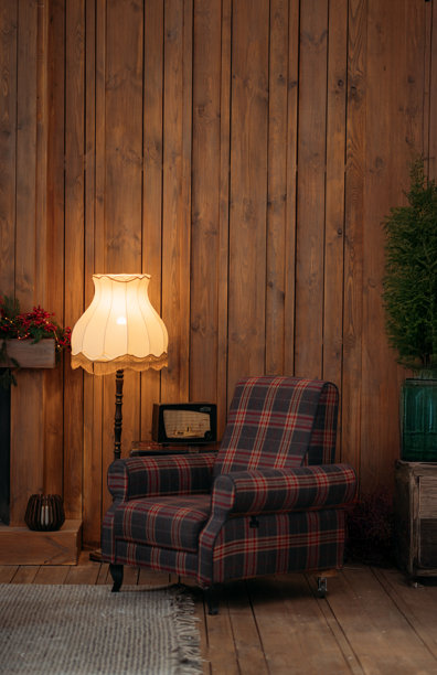 舒适的阅读角，格子扶手椅和复古台灯在质朴的客厅里温暖地发光，背景是木墙。图片下载