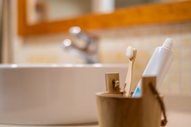 可持续口腔护理套装，包含竹制牙刷和牙膏，放置在浴室柜台上的支架中，背景为柔和模糊的水槽和水龙头，倡导环保、可生物降解的选择图片下载