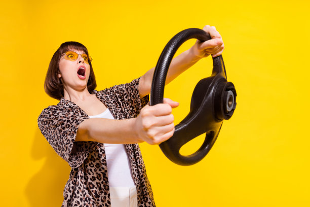 照片：一位戴着眼镜、穿着衬衫的年轻女子，惊奇地驾驶着，孤立在黄色背景上图片下载