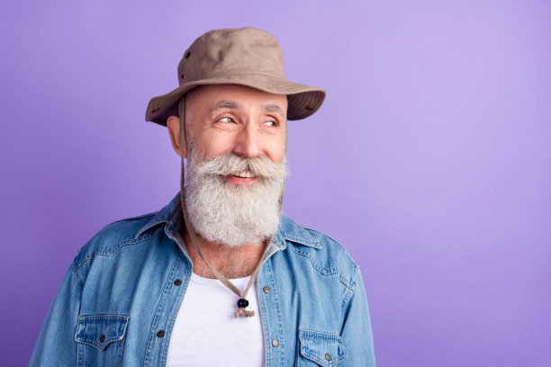 照片：一位戴着帽子、面带快乐积极微笑的老年男性游客，在紫色背景上图片下载