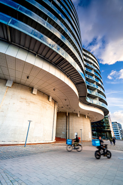 丹麦哥本哈根，人们骑着自行车经过一座未来感的玻璃住宅建筑的垂直照片。图片下载
