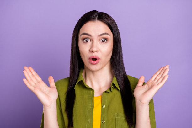 照片：迷人的年轻女子身穿卡其色服装，睁大眼睛，双臂高举，在孤立的紫色背景前，显得印象深刻。图片下载