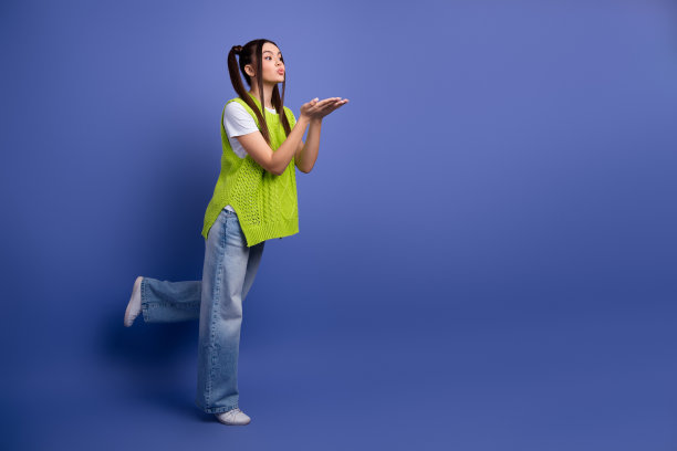 身穿亮绿色针织背心的年轻女子在蓝色影棚背景前飞吻，休闲时尚生活方式图片图片下载