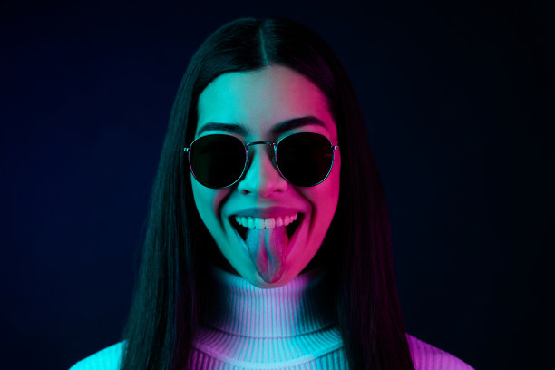 照片：一个年轻快乐的女孩，带着积极的微笑，吐着舌头，表情夸张，孤立在深色背景上。图片下载