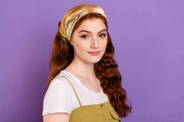 戴着头巾、留着姜黄色头发的平静安宁的年轻女子照片，背景为紫色和紫罗兰色。图片下载