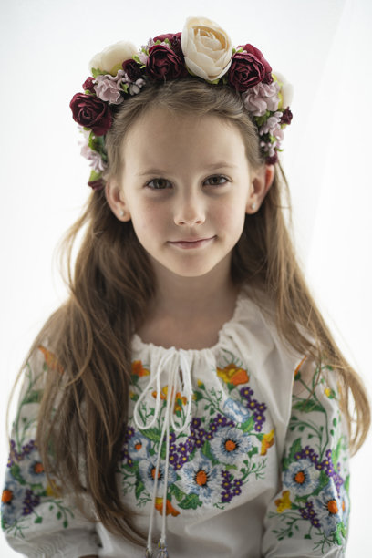 一名戴着花环、身穿白色刺绣衬衫的乌克兰女孩，面带微笑，站立在白色背景前，展现了童年和乌克兰传统。这是一张竖构图的照片。图片下载